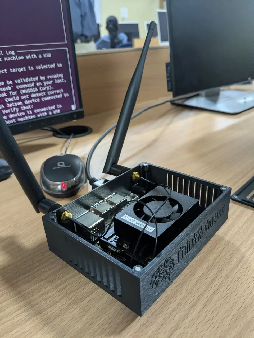 NVIDIA Jetson Nano board in a case with antennas, next to a monitor showing a terminal